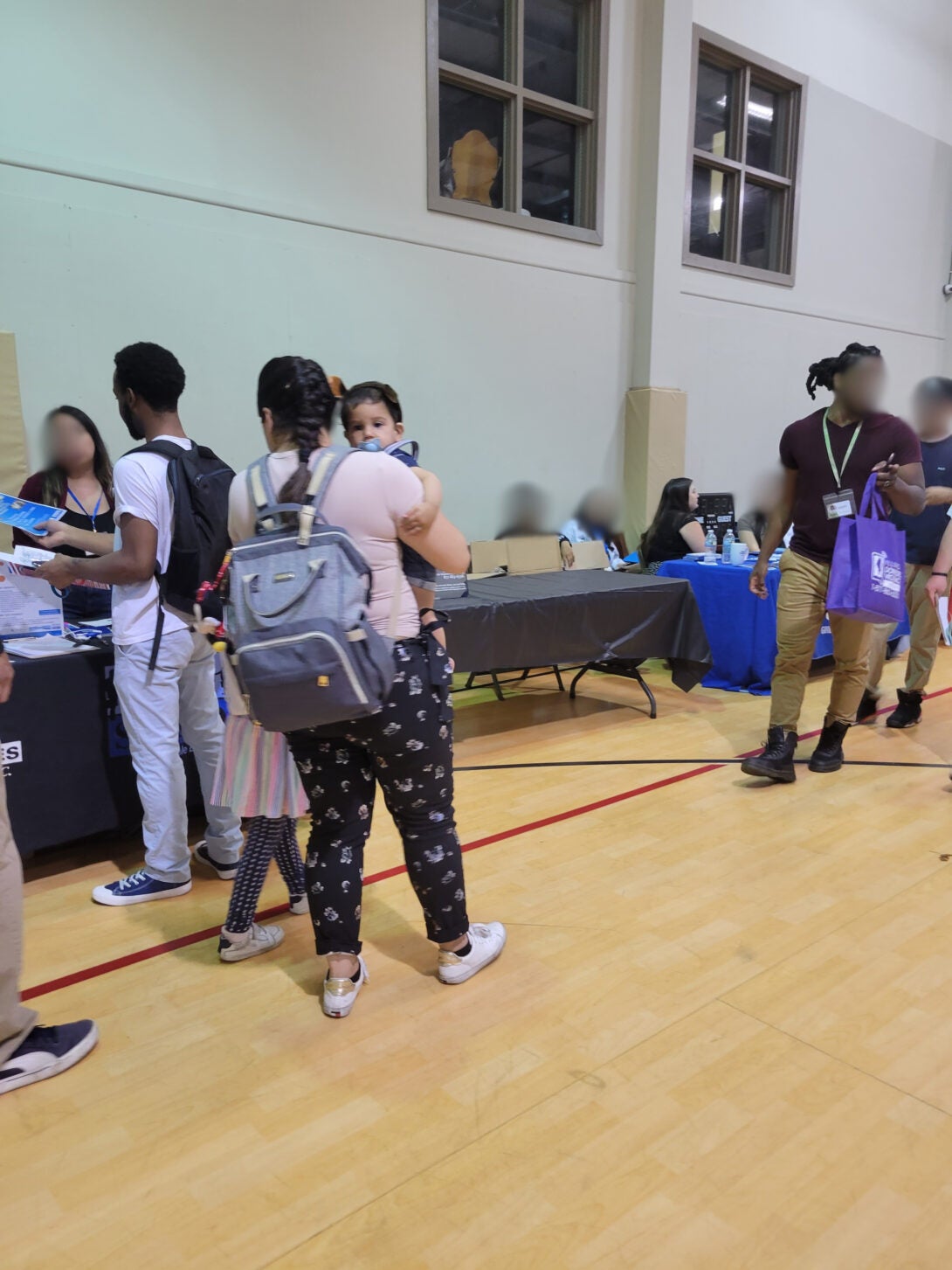 A mother facing away from the camera holds an infant. She is in a school gymnasium hosting a professional event.