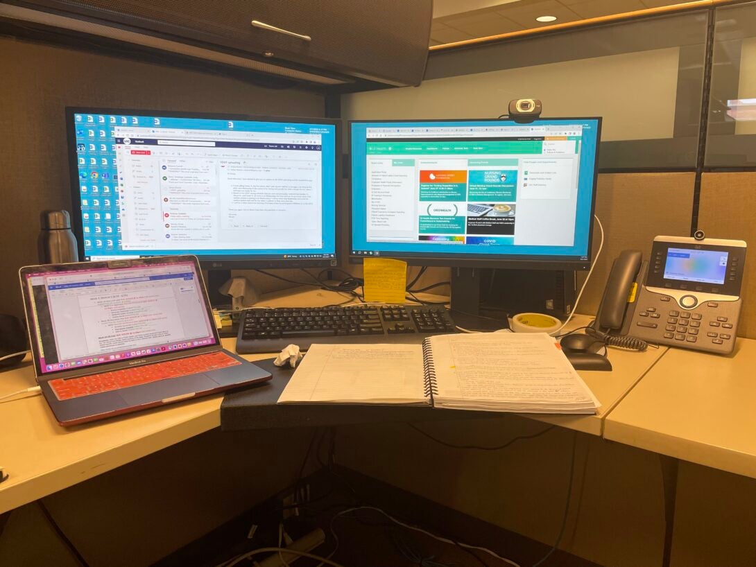 Several monitors display different work tasks inside an office cubicle