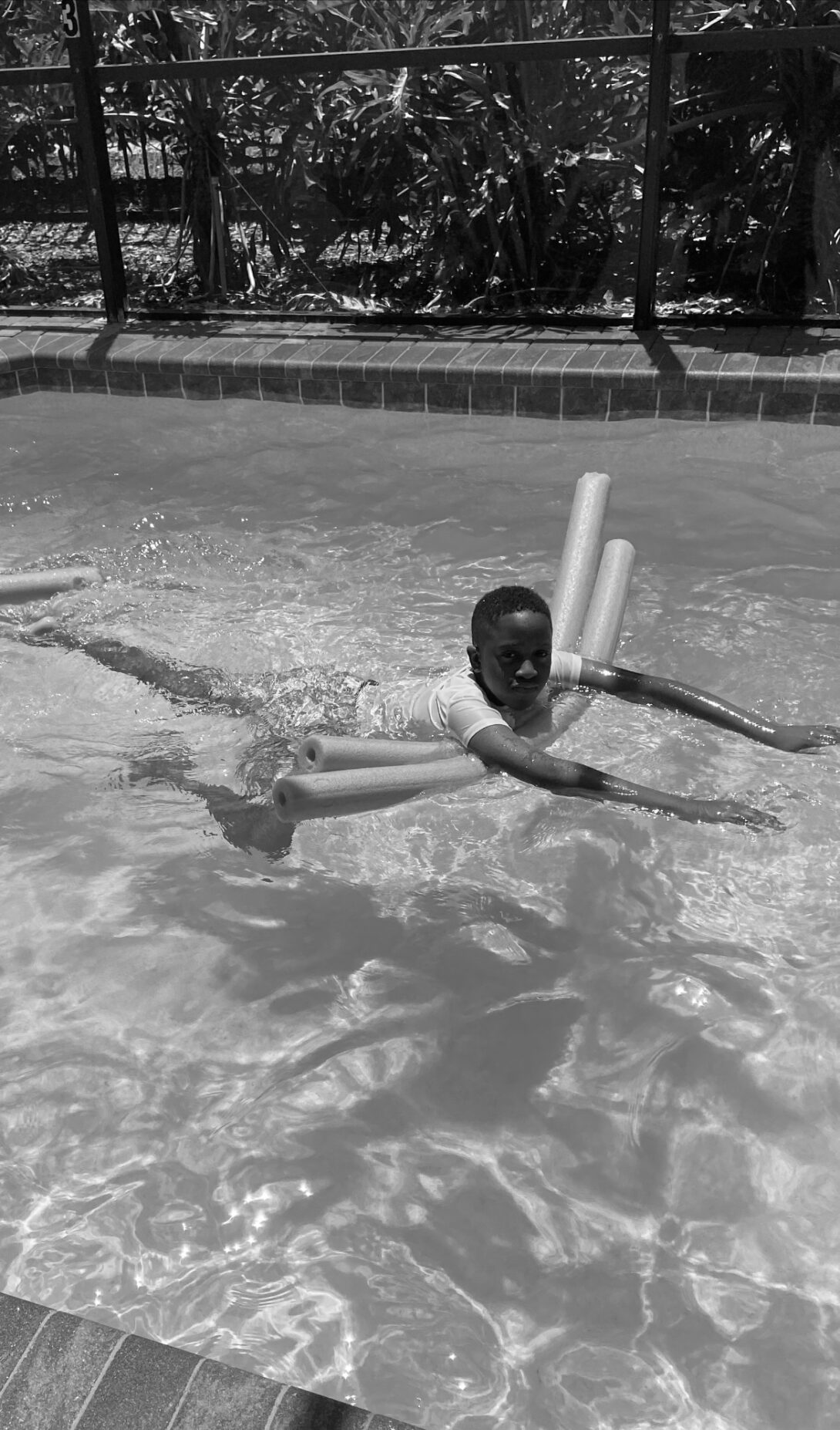 A young boy swims in a pool using pool noodles